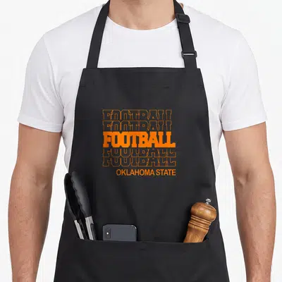 Football modern apron - Six stacked orange FOOTBALL texts with solid distressed center and smaller OKLAHOMA STATE below — shown on a black cotton canvas apron against a white background