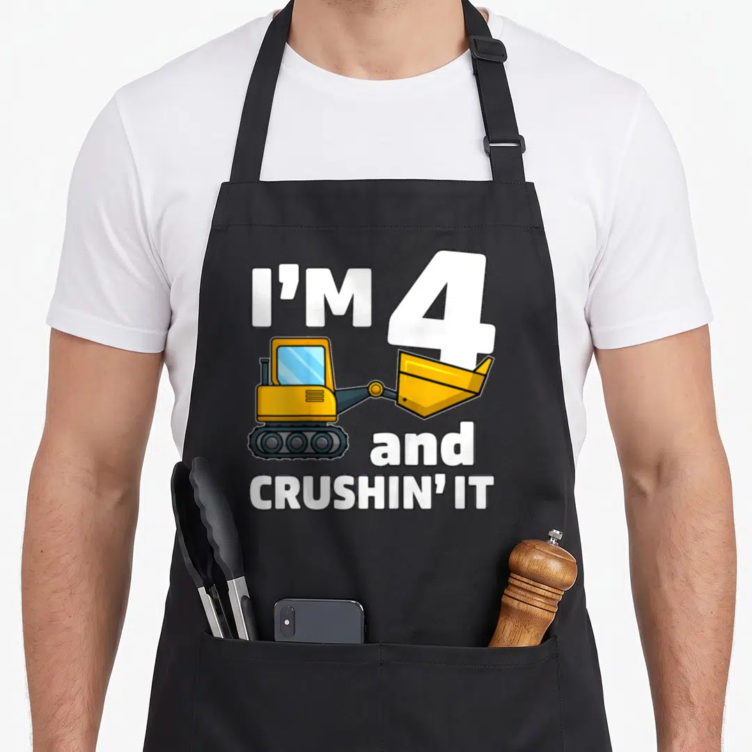 Construction 4th truck apron - Cartoon excavator with I'M 4 and CRUSHIN' IT text in white and yellow — shown on a black cotton canvas apron against a white background