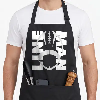 Defensive football apron - Vertical white LINE MAN text with grey football helmet graphic on grey background — shown on a black cotton canvas apron against a white background