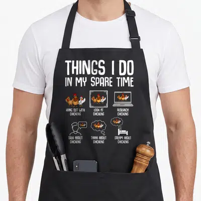 Funny spare chicken apron - Cartoon chickens standing and on laptop with text Things I Do In My Spare Time — shown on a black cotton canvas apron against a white background