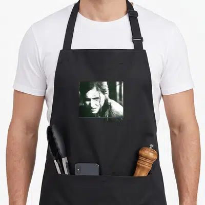 Ellie boxed us aprons - Square B&W photo of woman above right-aligned The Last of Us Part II text — shown on a black cotton canvas apron against a white background