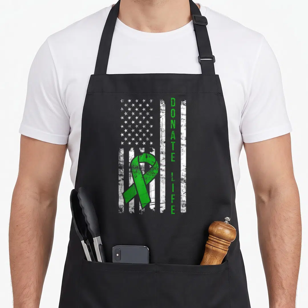 Distressed organ apron - Green ribbon and vertical Donate Life text on distressed white flag — shown on a black cotton canvas apron against a white background