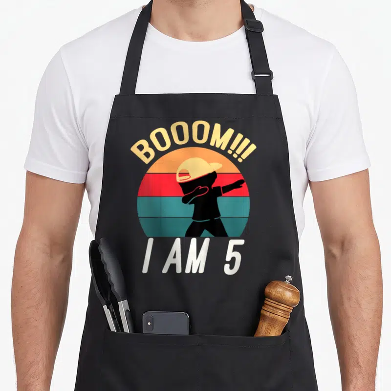 Funny dabbing birthday apron - Retro silhouette dabbing inside striped circle with BOOOM and I AM 5 text — shown on a black cotton canvas apron against a white background