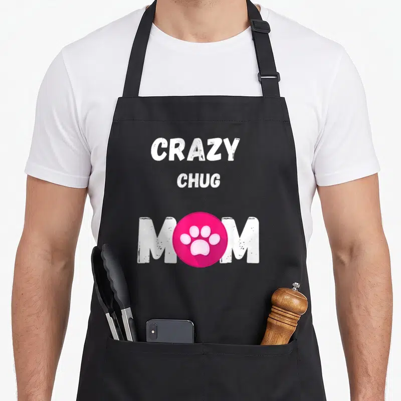 Funny chug cooking with dog apron - White text Crazy Chug Mom with pink paw print circle replacing the O — shown on a black cotton canvas apron against a white background