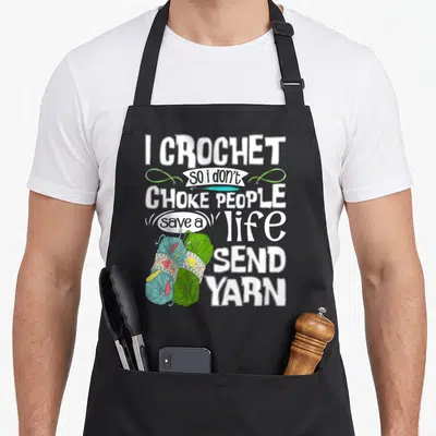Choke crocheting crochet apron - I CROCHET so i don't CHOKE PEOPLE save a life SEND YARN with blue and green yarn balls — shown on a black cotton canvas apron against a white background