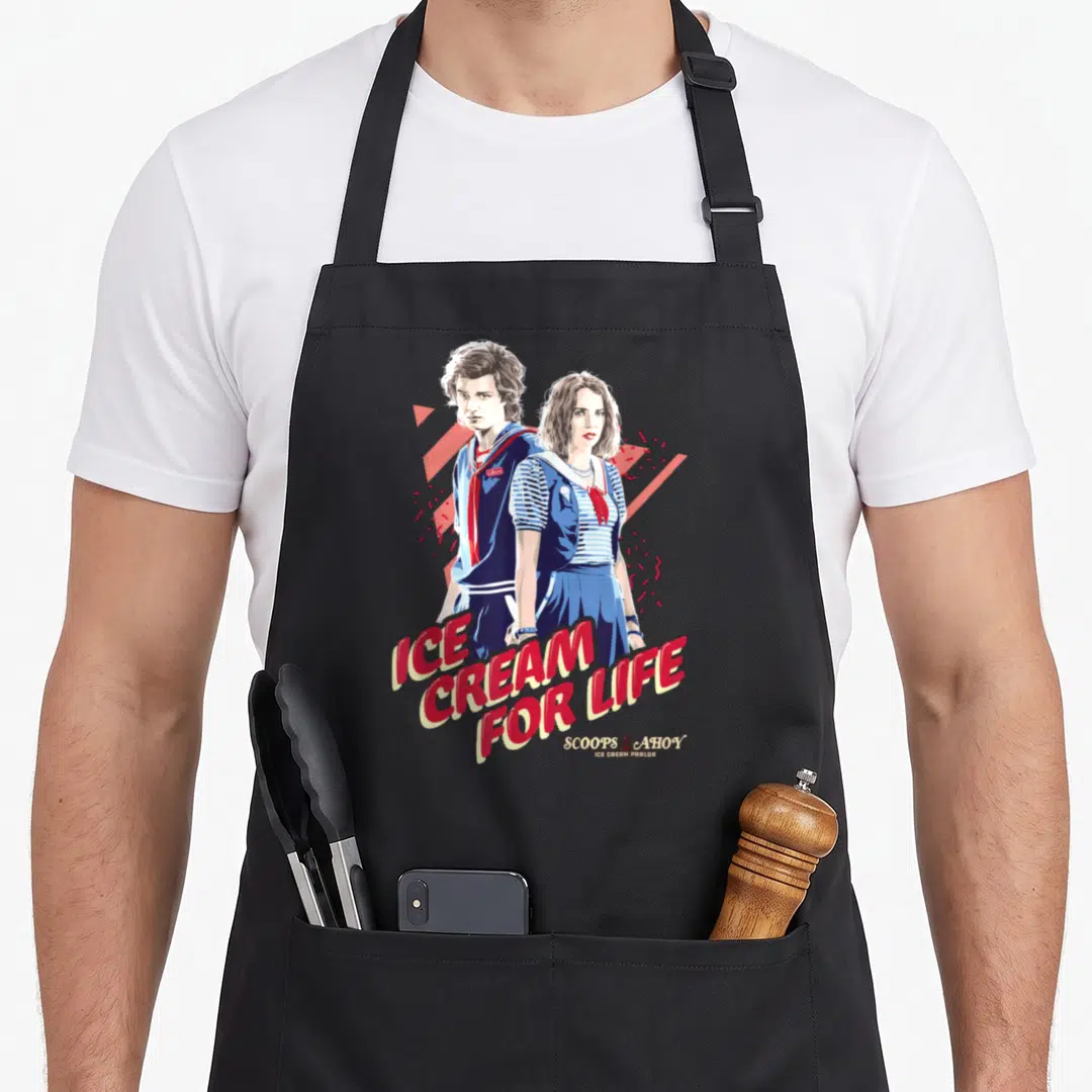 Steve ice cream apron - Two cartoon figures in blue uniforms with red text reading ICE CREAM FOR LIFE and geometric — shown on a black cotton canvas apron against a white background