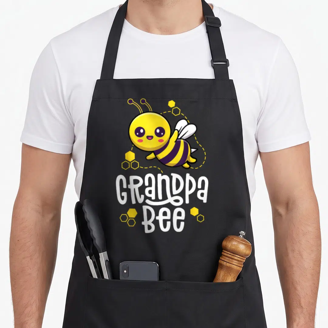 Grandpa bee aprons - Cartoon bee flying above white Grandpa Bee text surrounded by yellow honeycombs — shown on a black cotton canvas apron against a white background