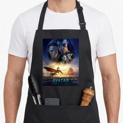 Avatar 20th century studios apron - Four Na'vi faces above an Ikran rider over ocean with AVATAR THE WAY OF WATER text — shown on a black cotton canvas apron against a white background