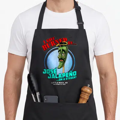 Jose trailer guy apron - Cartoon green jalapeno on stick wearing sombrero with red and cyan text inside blue circle — shown on a black cotton canvas apron against a white background