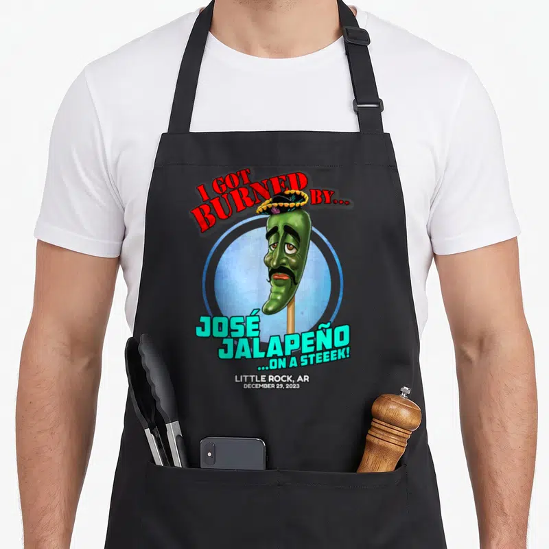 Jose trailer guy apron - Cartoon green jalapeno on stick wearing sombrero with red and cyan text inside blue circle — shown on a black cotton canvas apron against a white background