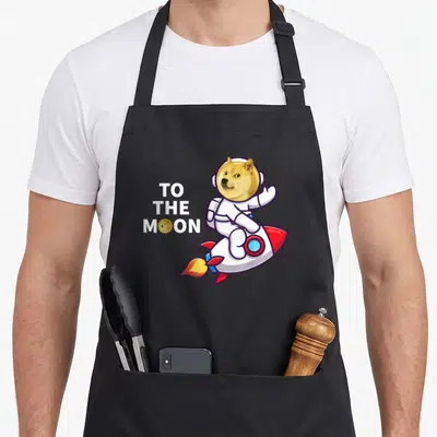 Dogecoin crypto apron - TO THE MOON text with astronaut dog on rocket and coin icon — shown on a black cotton canvas apron against a white background
