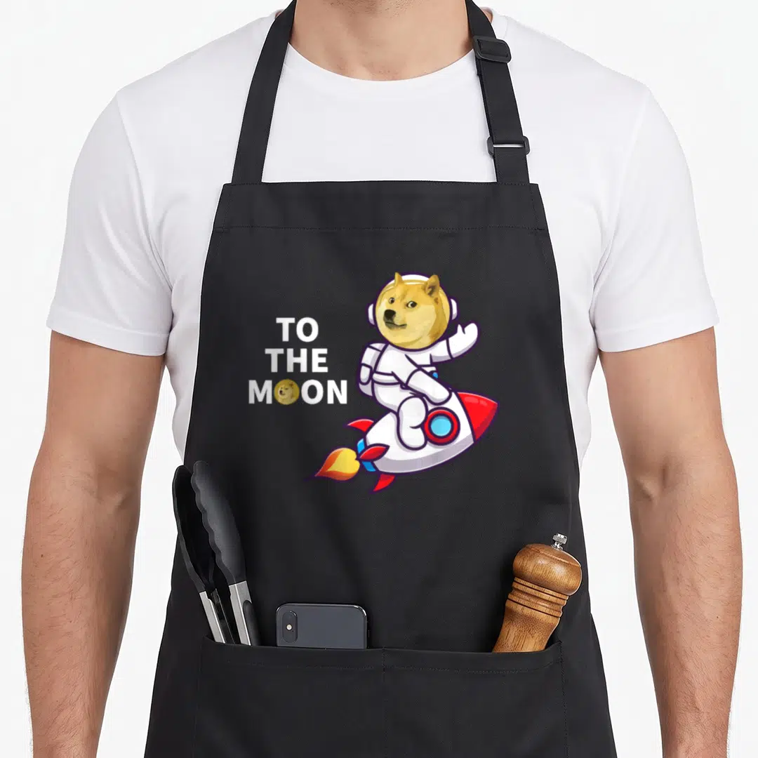 Dogecoin crypto apron - TO THE MOON text with astronaut dog on rocket and coin icon — shown on a black cotton canvas apron against a white background