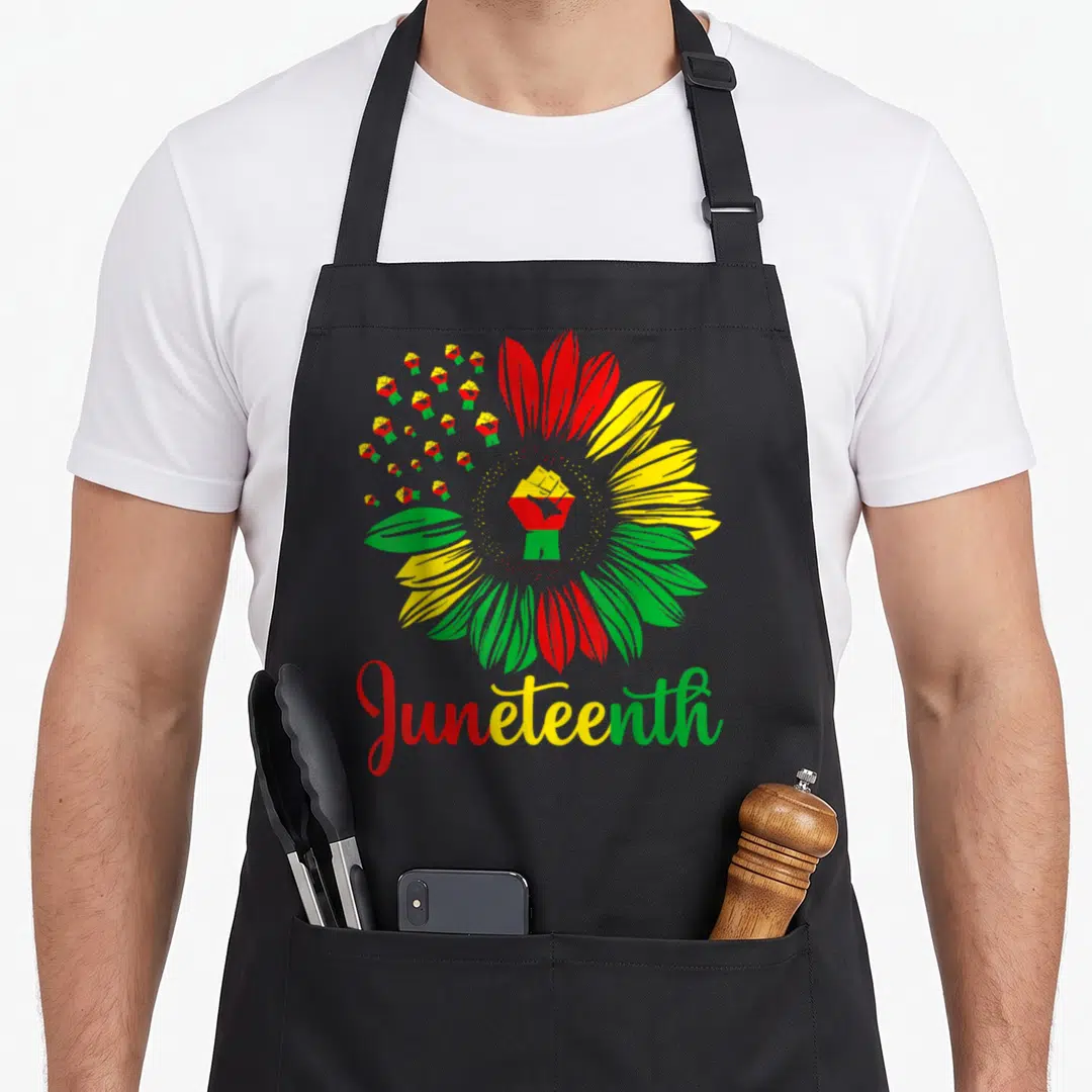 Juneteenth sunflower apron - Raised fist inside red yellow green flower with graduation caps and Juneteenth script — shown on a black cotton canvas apron against a white background