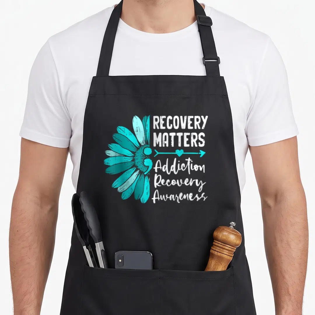 Awareness alcohol recovery apron - Teal daisy flower next to Recovery Matters text and arrow heart symbol in distressed — shown on a black cotton canvas apron against a white background