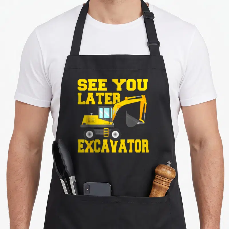 See birthday apron - Yellow excavator cartoon with See You Later Excavator text stacked vertically — shown on a black cotton canvas apron against a white background
