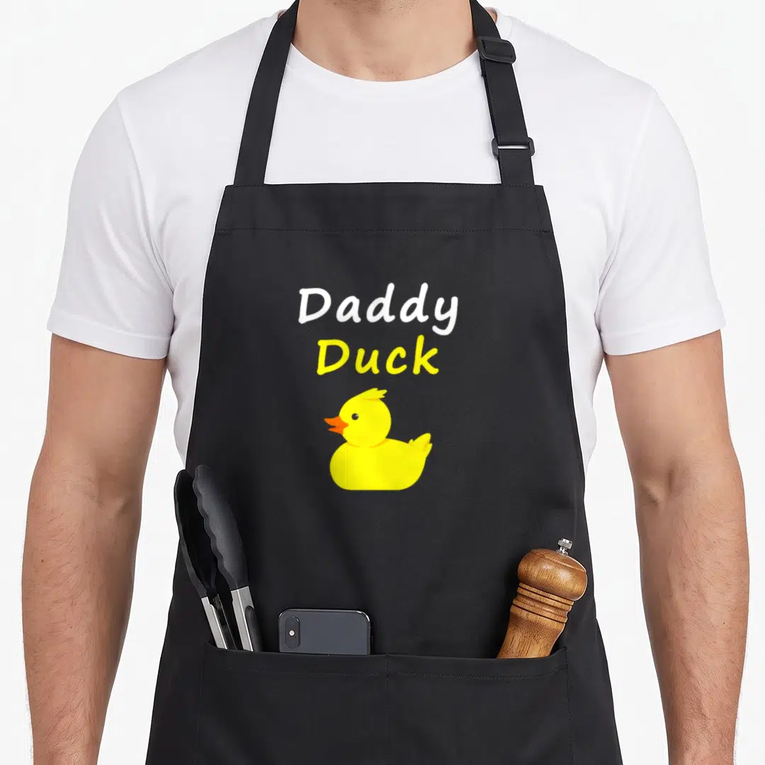 Rubber cotton duck apron - Stacked Daddy Duck text above a yellow cartoon rubber duck — shown on a black cotton canvas apron against a white background