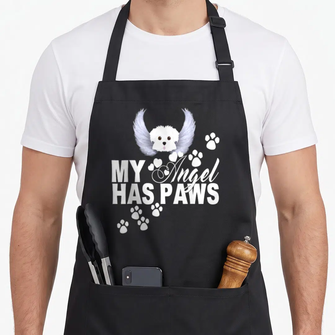 Angel dog apron - Winged white cartoon dog head with MY Angel Has Paws text and paw prints — shown on a black cotton canvas apron against a white background