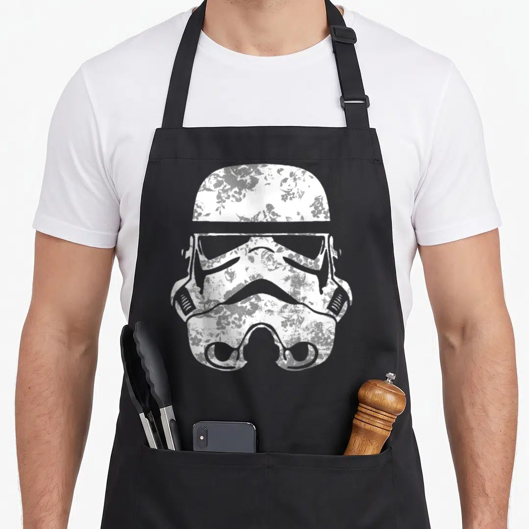 Fill floral apron - White stormtrooper helmet filled with distressed floral pattern on gray background — shown on a black cotton canvas apron against a white background