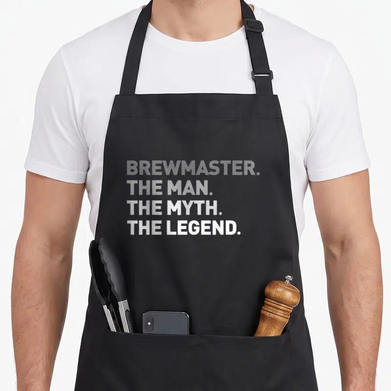 Brewmaster craft apron - Stacked white text reading BREW MASTER THE MAN THE MYTH THE LEGEND on grey background — shown on a black cotton canvas apron against a white background