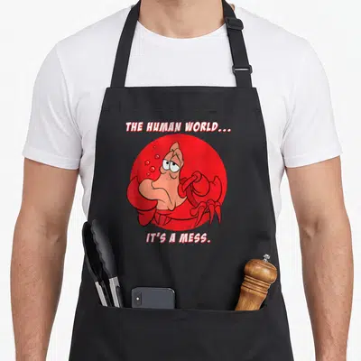 Sebastian mermaid apron - Crab inside red circle with text THE HUMAN WORLD IT'S A MESS — shown on a black cotton canvas apron against a white background