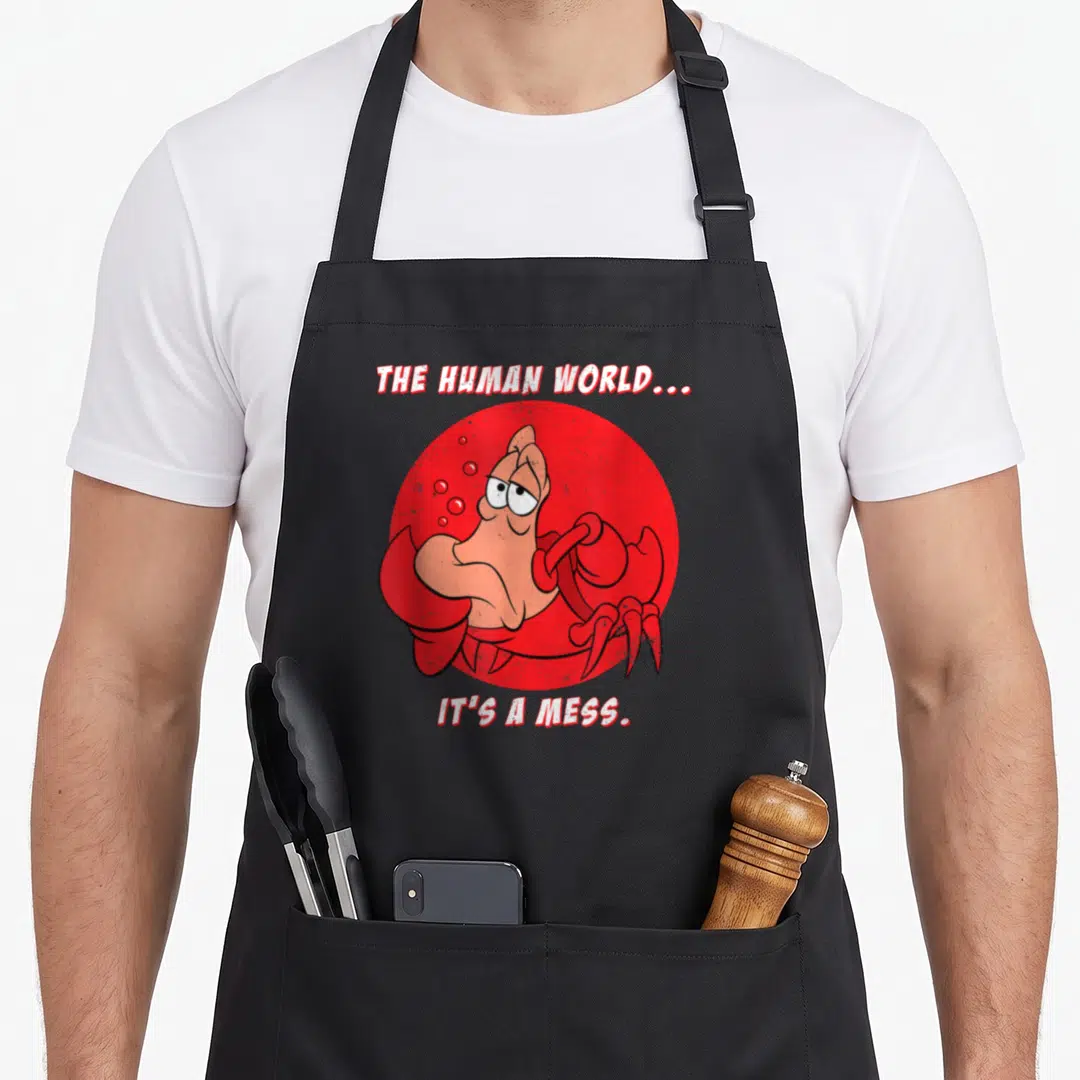 Sebastian mermaid apron - Crab inside red circle with text THE HUMAN WORLD IT'S A MESS — shown on a black cotton canvas apron against a white background