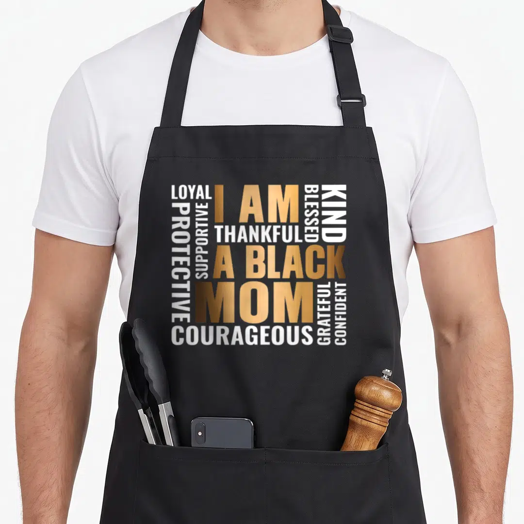 Positive history mom apron - I AM A BLACK MOM text block in gold and white with surrounding affirmations — shown on a black cotton canvas apron against a white background