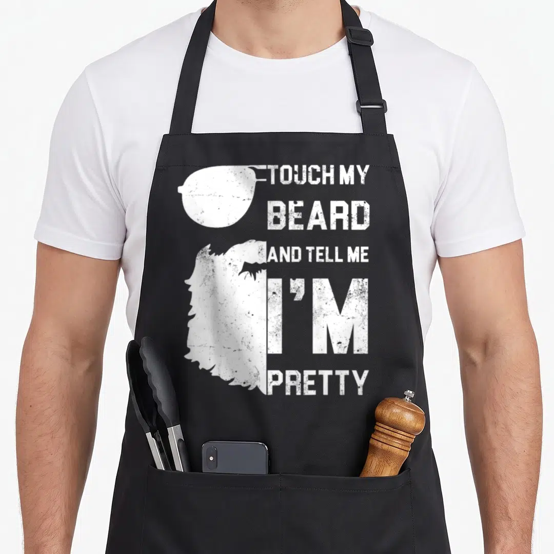 Touch father day apron - White distressed silhouette of sunglasses and beard next to stacked text touching my beard — shown on a black cotton canvas apron against a white background