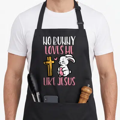 Bunny jesus easter apron - Cartoon white bunny holding pink heart beside yellow cross with NO BUNNY LOVES ME LIKE JESUS — shown on a black cotton canvas apron against a white background