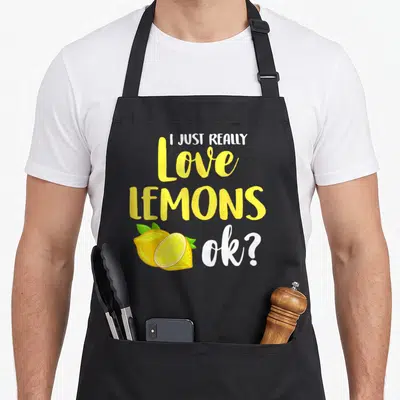 Juice lemonade apron - Stacked text I Just Really Love Lemons Ok with cartoon yellow lemons and green leaves — shown on a black cotton canvas apron against a white background