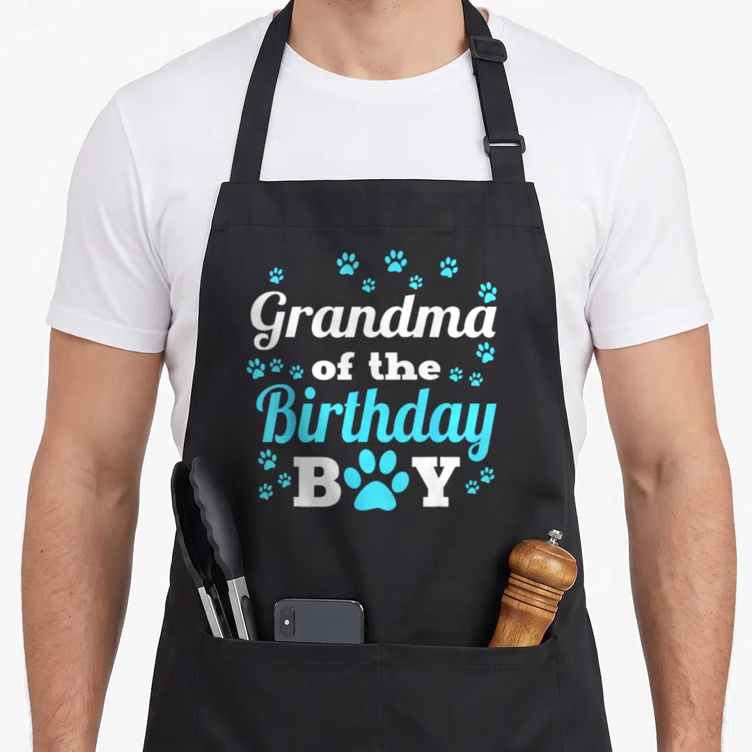 Bday dog apron - Grandma of the Birthday BOY text with white and blue paw prints — shown on a black cotton canvas apron against a white background