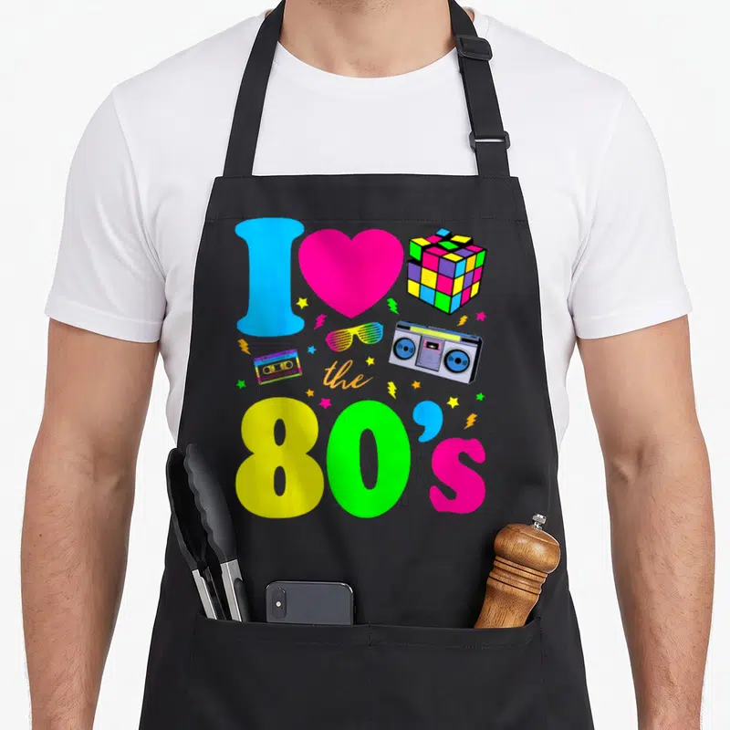 Clothe 80s apron - I love the 80s collage with boombox, cassette, Rubik's cube, and rainbow text — shown on a black cotton canvas apron against a white background