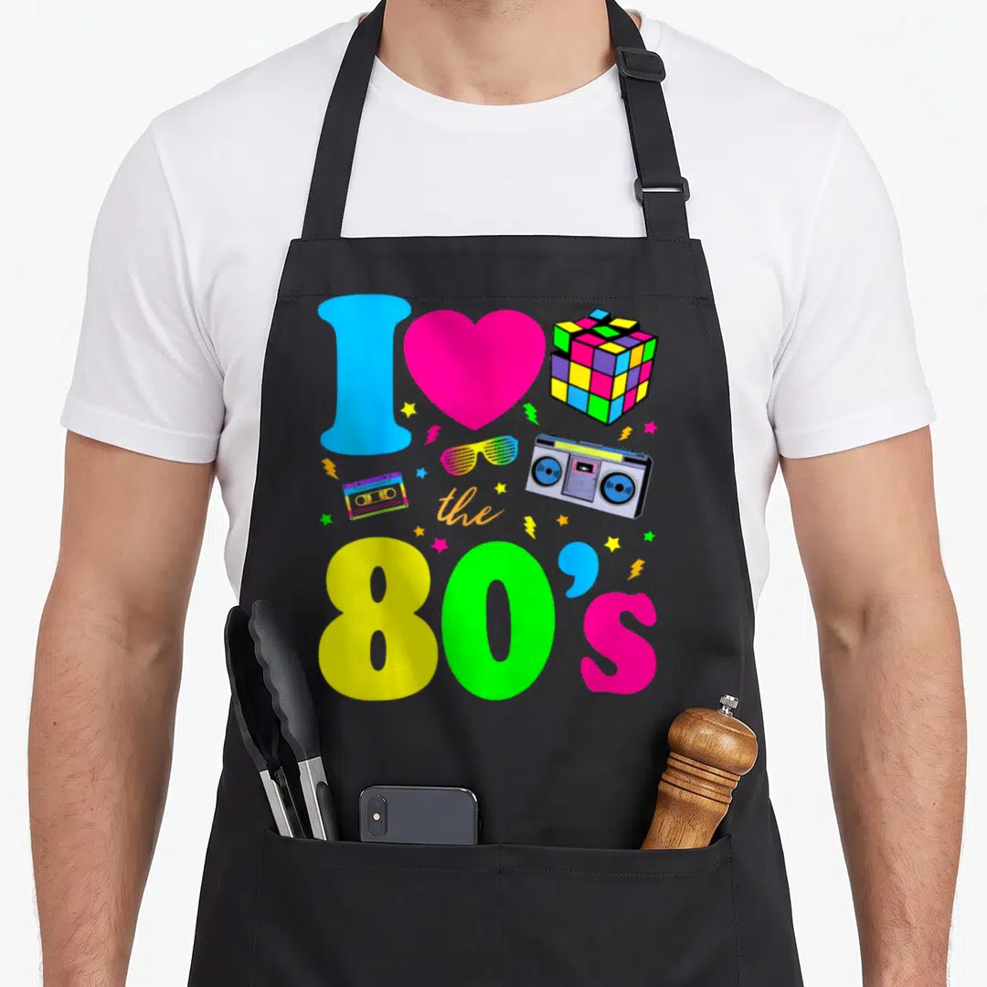 Clothe 80s apron - I love the 80s collage with boombox, cassette, Rubik's cube, and rainbow text — shown on a black cotton canvas apron against a white background