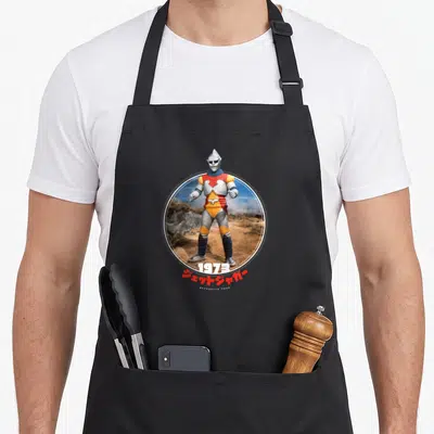 Jet animal apron - Circular photo of Jet Jaguar in silver red yellow armor with 1973 and Japanese text below — shown on a black cotton canvas apron against a white background