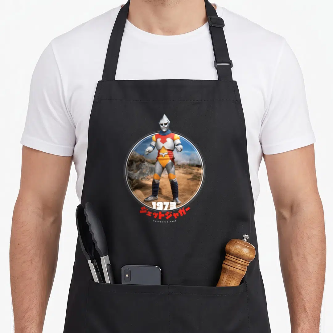 Jet animal apron - Circular photo of Jet Jaguar in silver red yellow armor with 1973 and Japanese text below — shown on a black cotton canvas apron against a white background