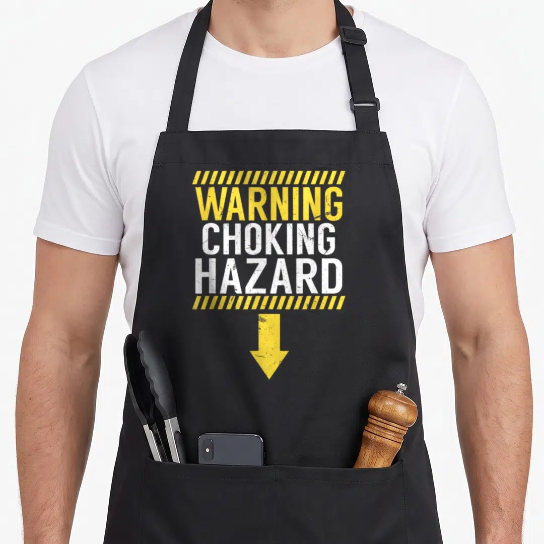 Warning joke apron - Distressed yellow and white warning sign text with stripes and downward arrow — shown on a black cotton canvas apron against a white background
