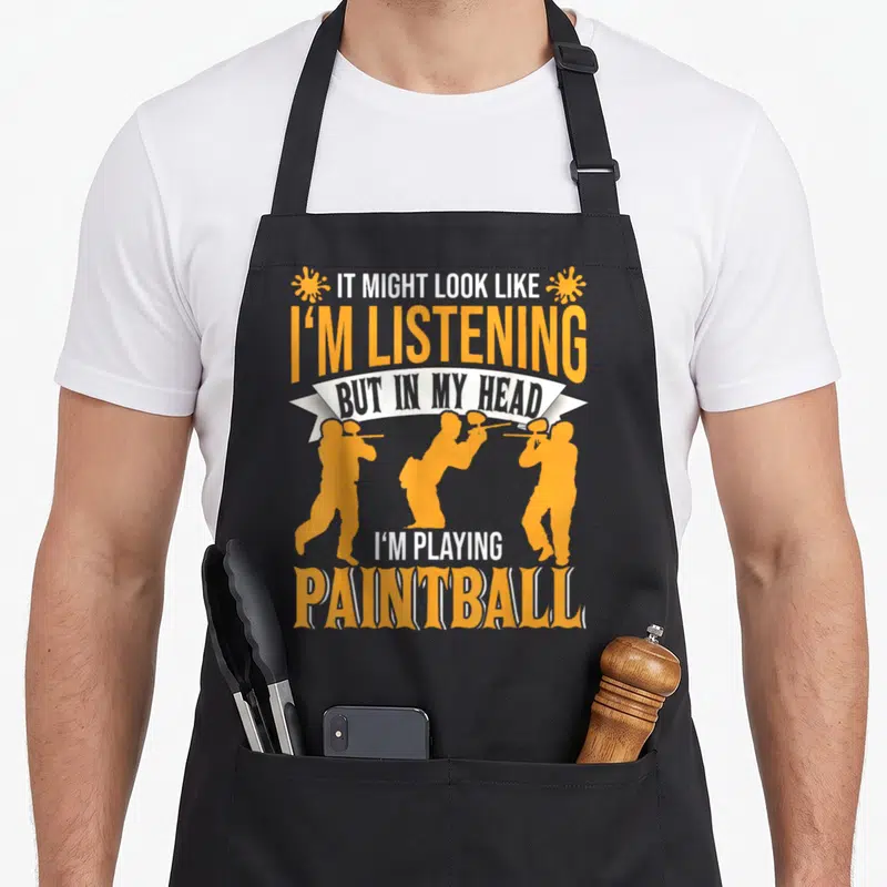 Funny paintball lover apron - Stacked orange and white text with three paintball player silhouettes and two splat — shown on a black cotton canvas apron against a white background