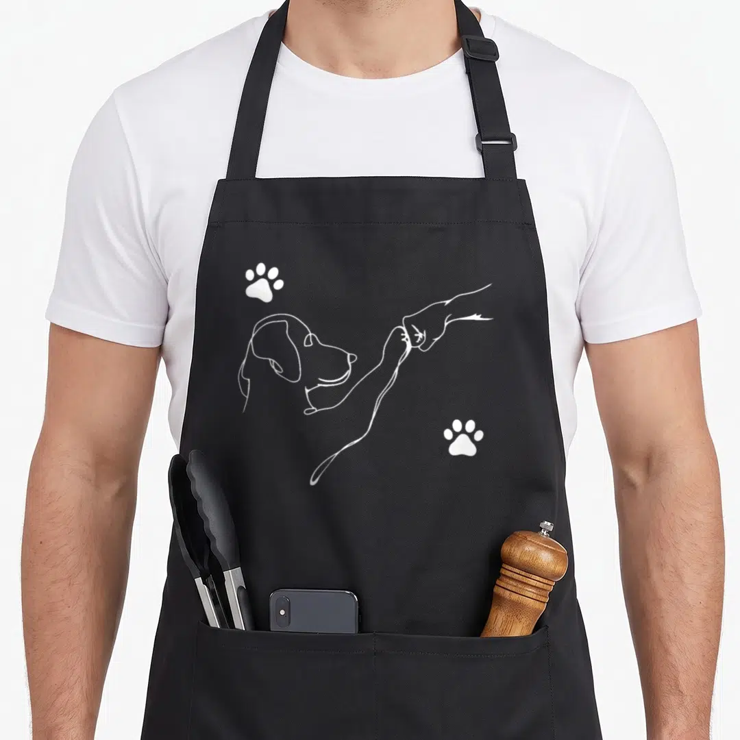 Hand dog apron - White line-art dog head and human hand fist bump with two paw prints — shown on a black cotton canvas apron against a white background