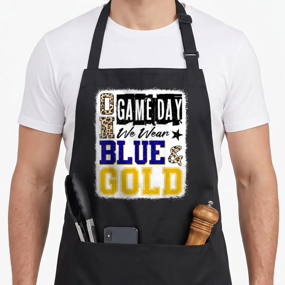 Gameday blue football apron - Stacked text ON GAME DAY We Wear BLUE & GOLD with spotted O and black star on white — shown on a black cotton canvas apron against a white background