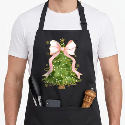 Coquette christmas tree apron - Green Christmas tree with pink bow, gold star, and snowflakes in watercolor style — shown on a black cotton canvas apron against a white background