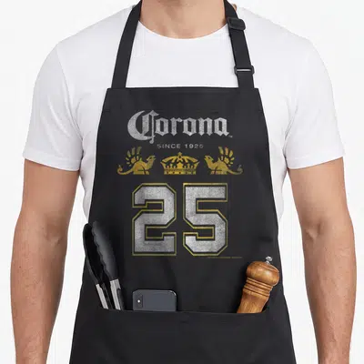 Corona logo officially apron - White and gold typography with crown, two birds, and large number 25 — shown on a black cotton canvas apron against a white background
