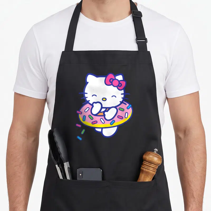 Floaty sprinkle apron - Hello Kitty standing in pink donut with blue yellow sprinkles and pink bow — shown on a black cotton canvas apron against a white background