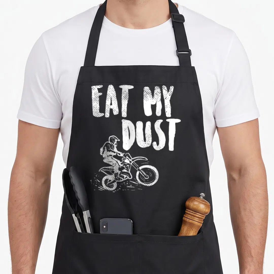 Eat motorcycle aprons - White EAT MY DUST text above motocross rider kicking up dust in distressed style — shown on a black cotton canvas apron against a white background