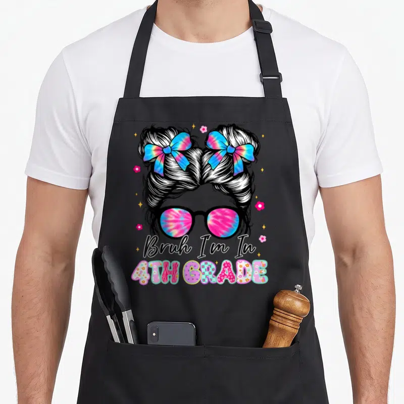Grade messy aprons - Cartoon messy bun with two tie-dye bows and glasses above text reading Bruh I'm In 4TH GRADE — shown on a black cotton canvas apron against a white background