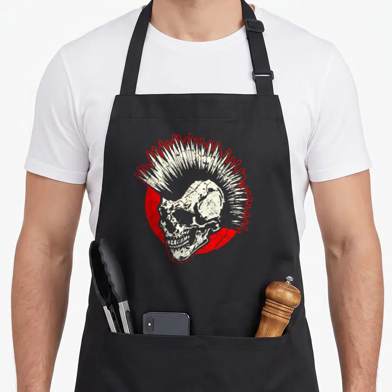 Funny music punk rock apron - Distressed white skull with mohawk on red circle, black bib — shown on a black cotton canvas apron against a white background