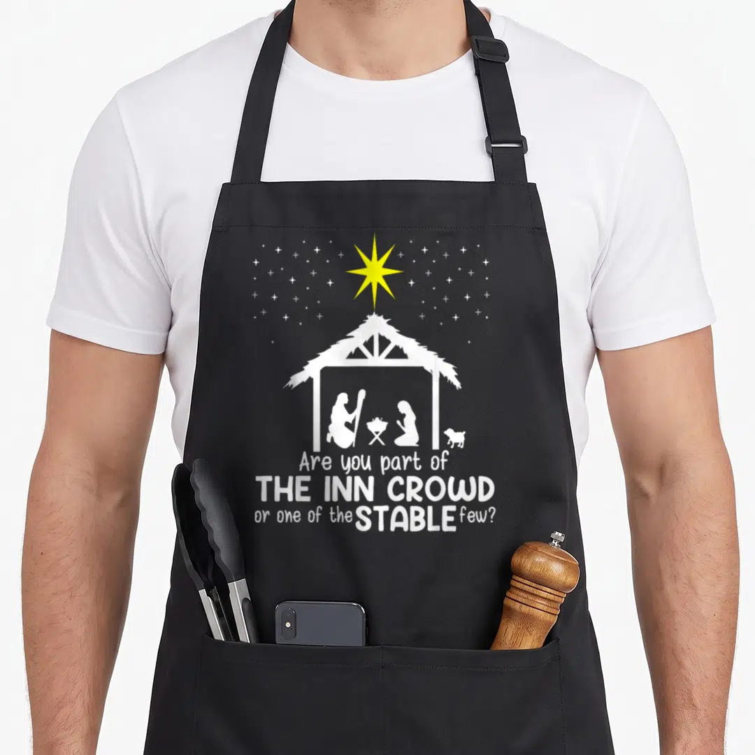 Inn womens christmas apron - White stable silhouette with yellow star and inn crowd stable few text — shown on a black cotton canvas apron against a white background