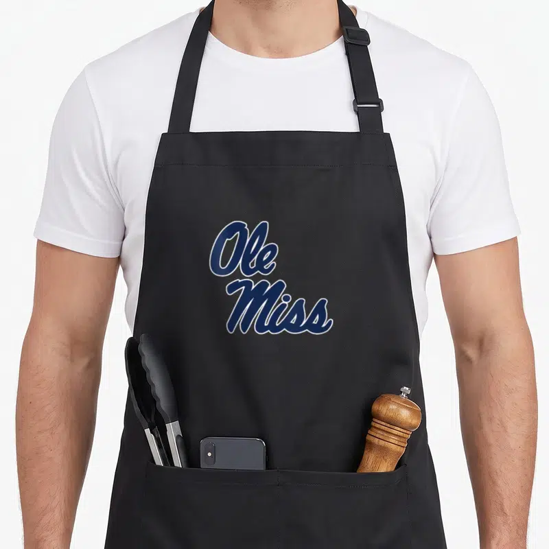 Ole mississippi apron - Stacked navy blue cursive Ole Miss text with white outline on canvas — shown on a black cotton canvas apron against a white background