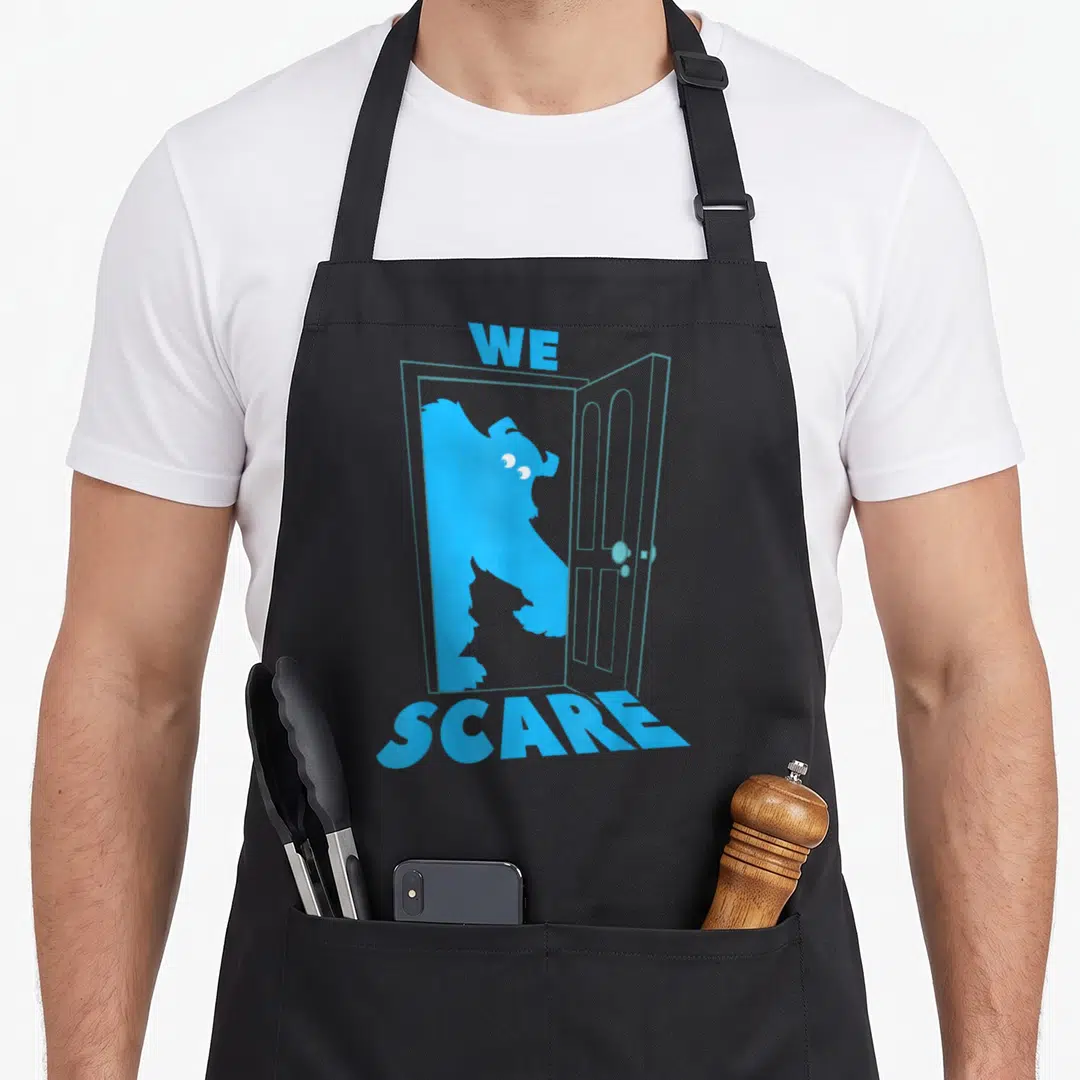 Sulley door apron - Blue We Scare text above and below door with monster silhouette inside — shown on a black cotton canvas apron against a white background