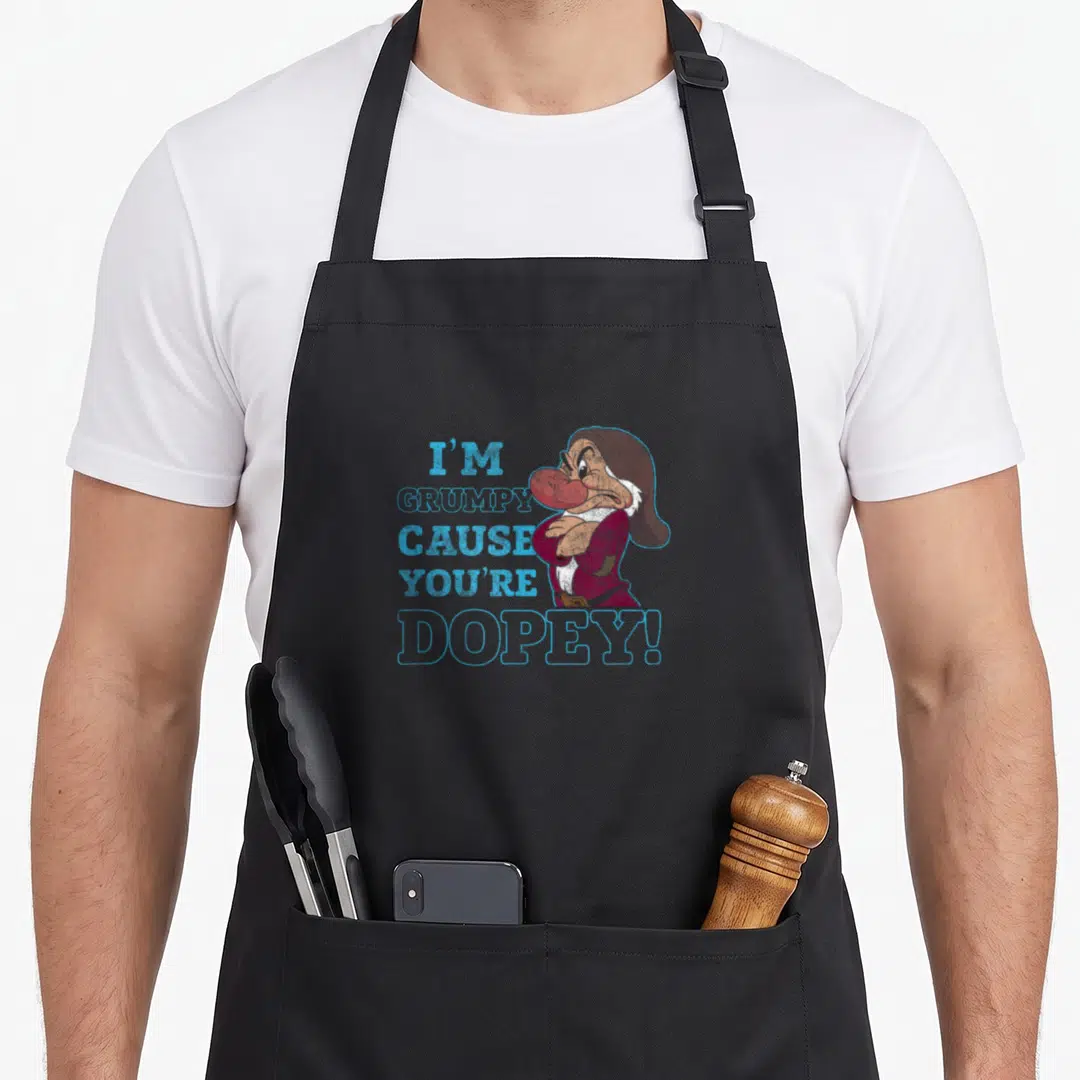 Grumpy dopey snow white apron - I'M GRUMPY CAUSE YOU'RE DOPEY! text with cartoon dwarf in blue red brown — shown on a black cotton canvas apron against a white background