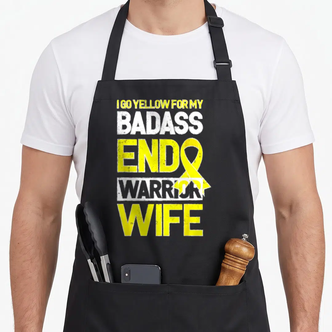 Endometriosis wife apron - Stacked yellow and white text reading I Go Yellow For My Badass Endo Warrior Wife — shown on a black cotton canvas apron against a white background