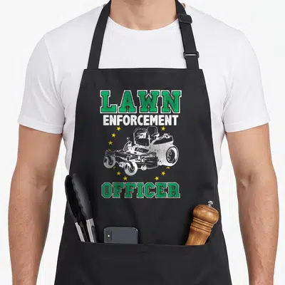 Enforcement rangers apron - LAWN ENFORCEMENT OFFICER text with white riding mower and yellow stars in distressed print — shown on a black cotton canvas apron against a white background